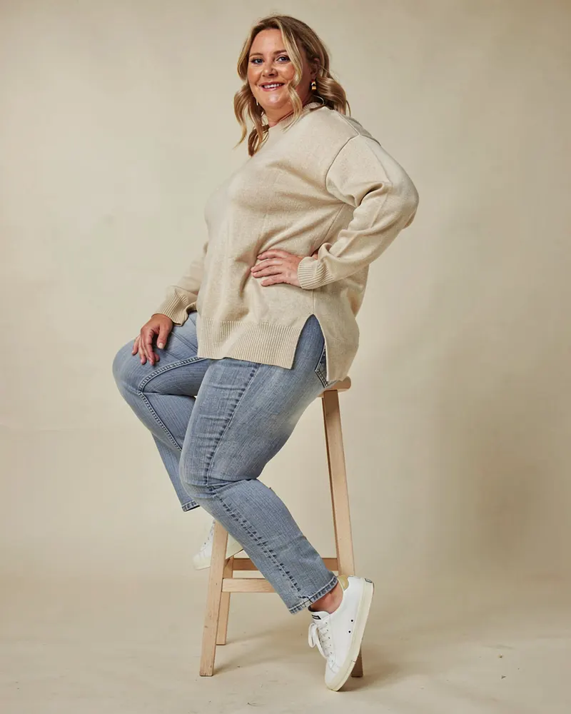 Knitted Lounge Jumper in Oatmeal, relaxed on a pale-oak stool in a warm studio
