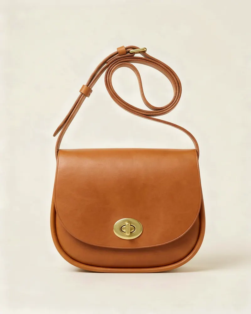 Sadie Leather Crossbody Bag in Tan, front view: a small saddle-shaped vegetable-tanned leather crossbody bag with a flap, a brass turn-lock and an adjustable strap
